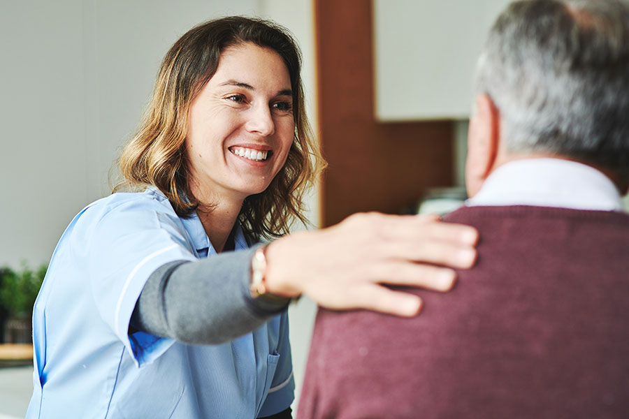 Hearing specialist with her hand on a man’s shoulder thanking them for being a loyal patient