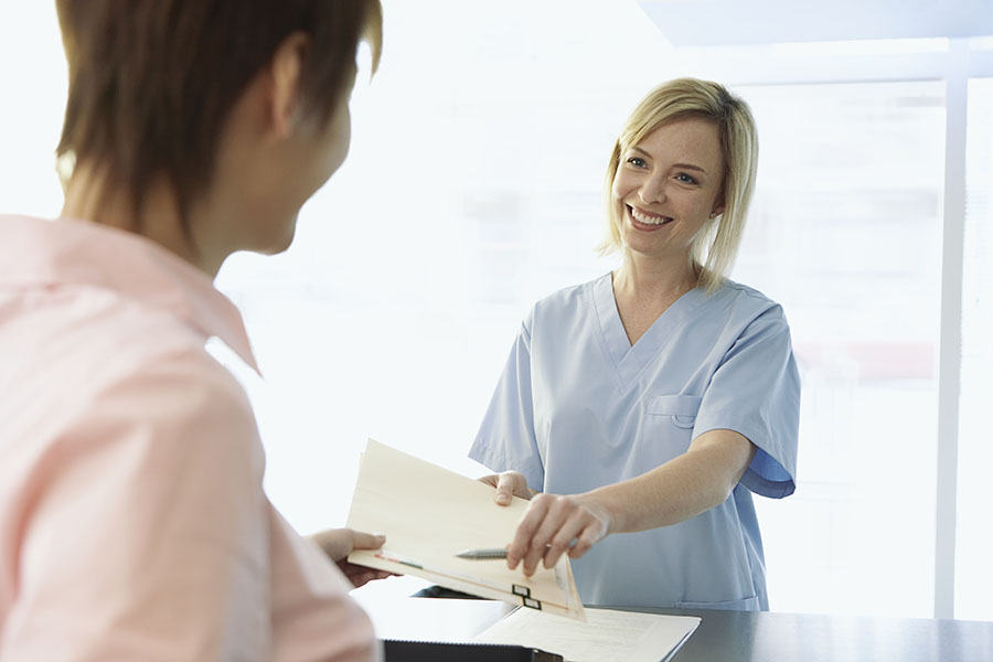 Woman working the front desk of an audiology practice providing a patient paperwork for their appointment.